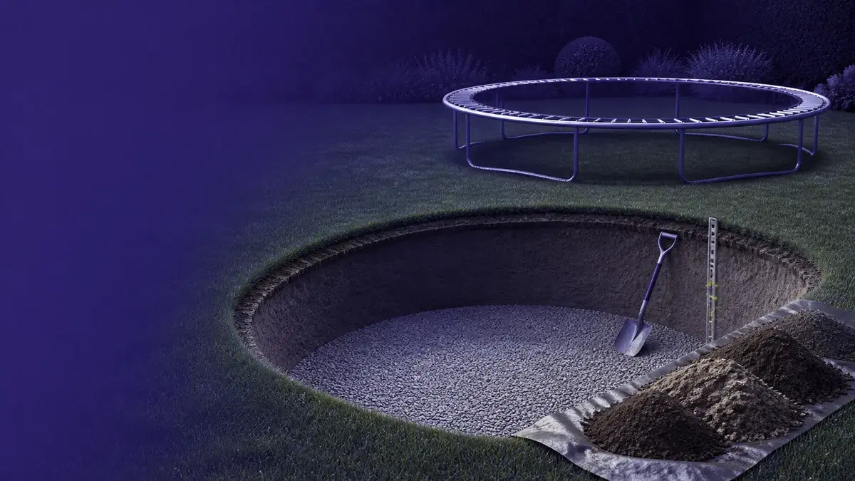 Færdiggravet trampolingrube med grusbund, skovl og ramme placeret på græsset